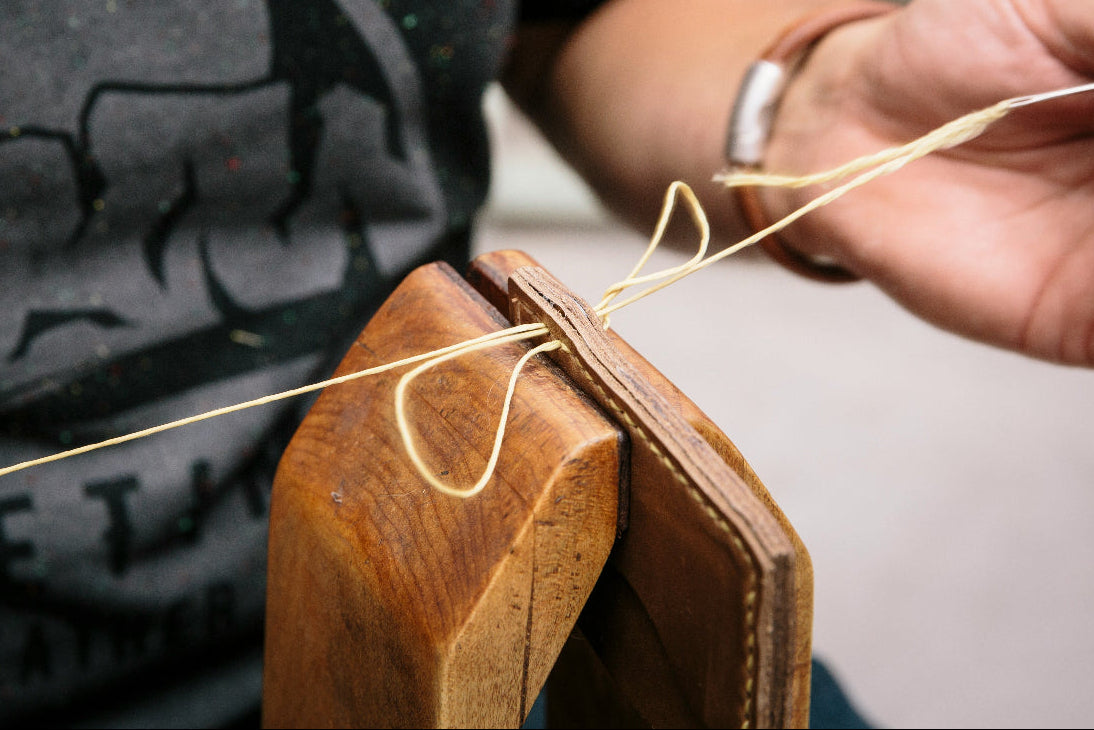 Person working with leather and thread, wearing a black shirt with a logo.